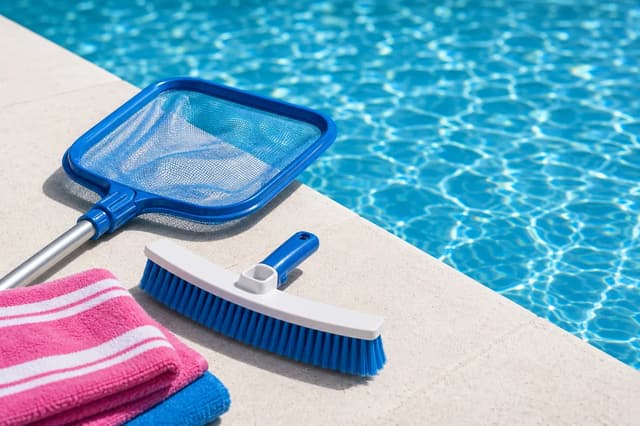 Leaf skimmer net and pool wall brush on the deck of a clear pool